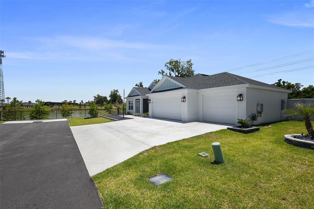 A white house with a two-car garage and a concrete driveway sits near a pond — 6716 BUDDY LANE, THE VILLAGES, FL