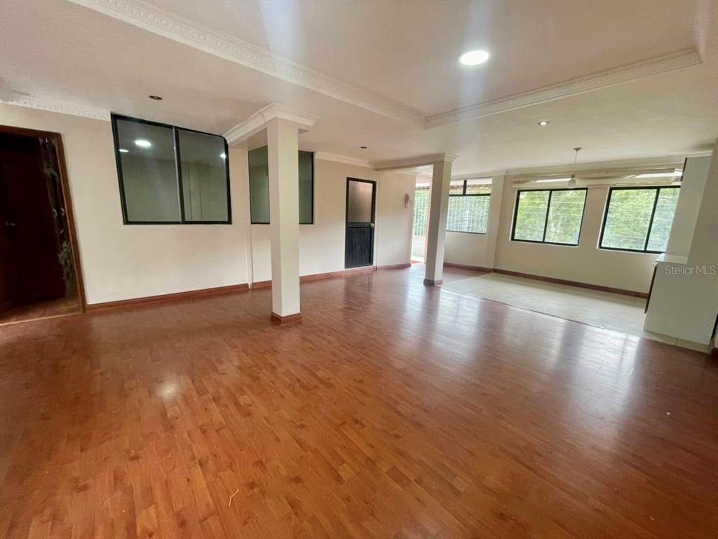 An open-concept living area features hardwood flooring, white walls, support columns, and large windows — 77 FRANCISCO LECARO, LOJA/ECUADOR, OC