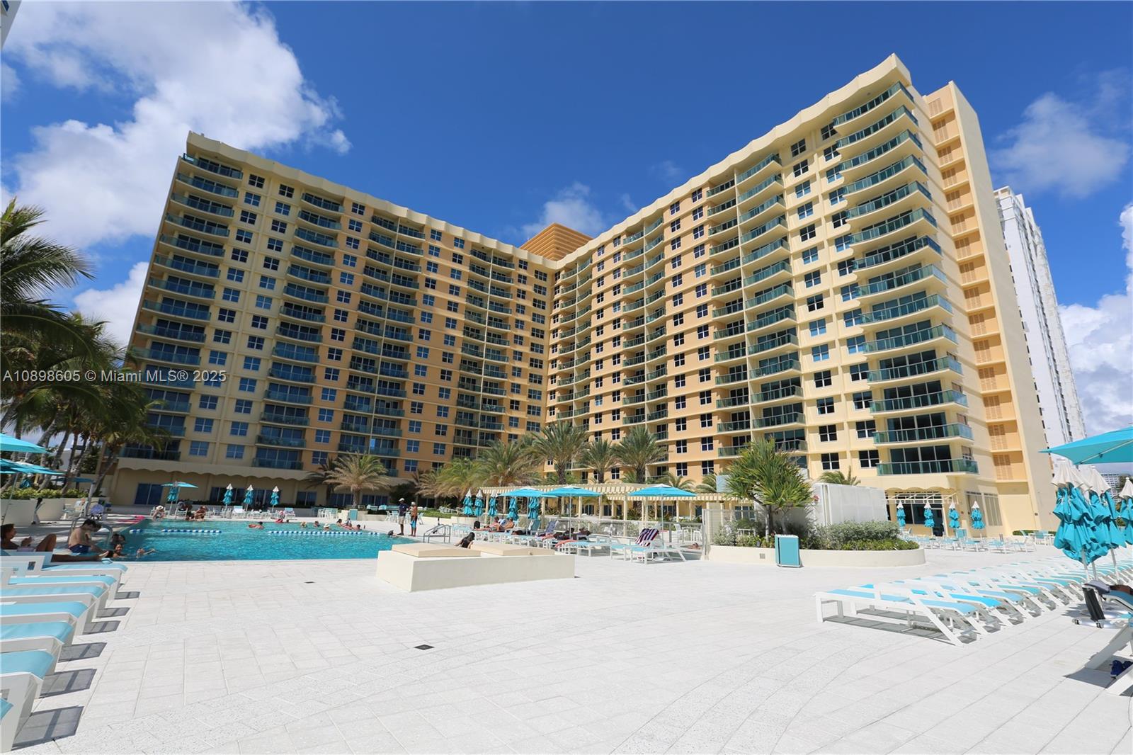 A large, multi-story yellow residential building stands behind a swimming pool with lounge chairs — 2501 S Ocean Dr, Hollywood FL 33019, HOLLYWOOD, FL
