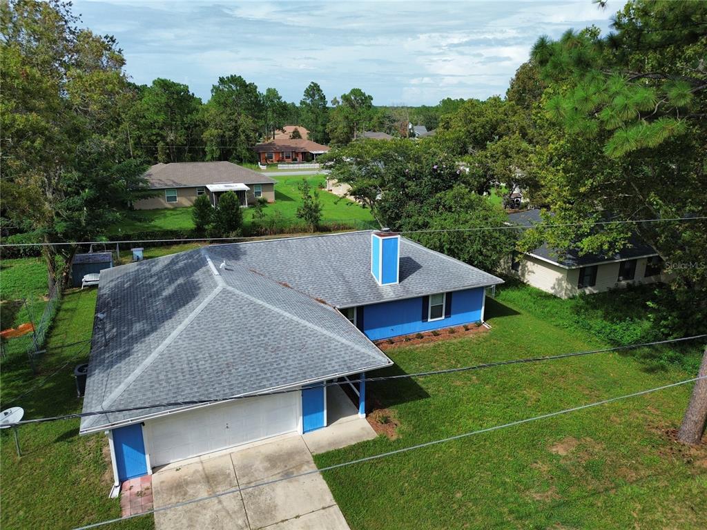 An aerial view of a blue single-story house with a gray shingled roof and driveway — 11 FIR TRAIL TRACK, OCALA, FL