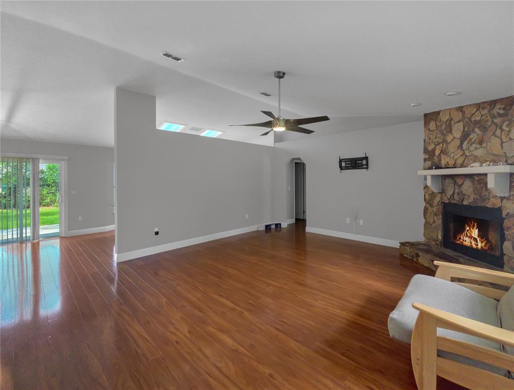 A living room with hardwood floors, a stone fireplace, and a ceiling fan — 11 FIR TRAIL TRACK, OCALA, FL