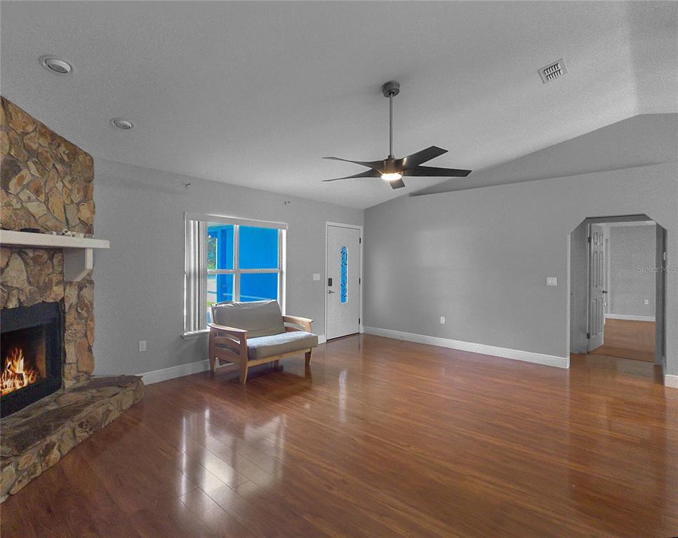 A living room features a stone fireplace, wood flooring, a ceiling fan, and a front door — 11 FIR TRAIL TRACK, OCALA, FL