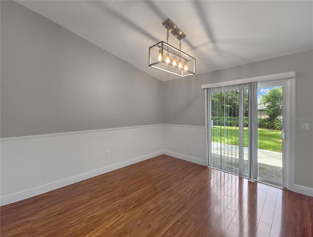 A dining room features wood flooring, gray walls with white wainscoting, a modern chandelier, and sliding glass doors — 11 FIR TRAIL TRACK, OCALA, FL