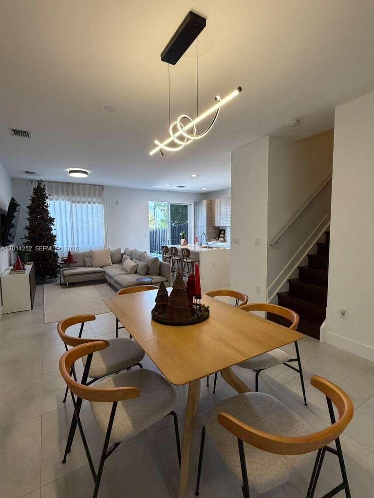 An open-concept dining and living area features a modern light fixture and wooden furniture — 7187 NW 103 PATH # 7187, Miami FL 33178, MIAMI, FL