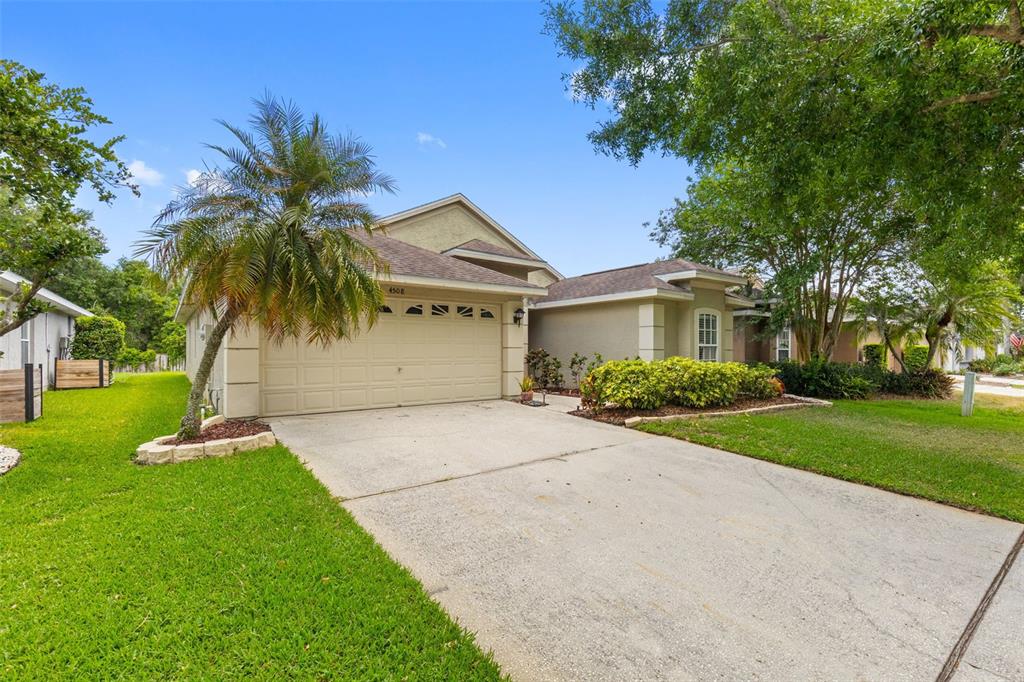 A beige single-story house with a two-car garage, a concrete driveway, and a palm tree — 4508 NEW DAWN COURT, LUTZ, FL