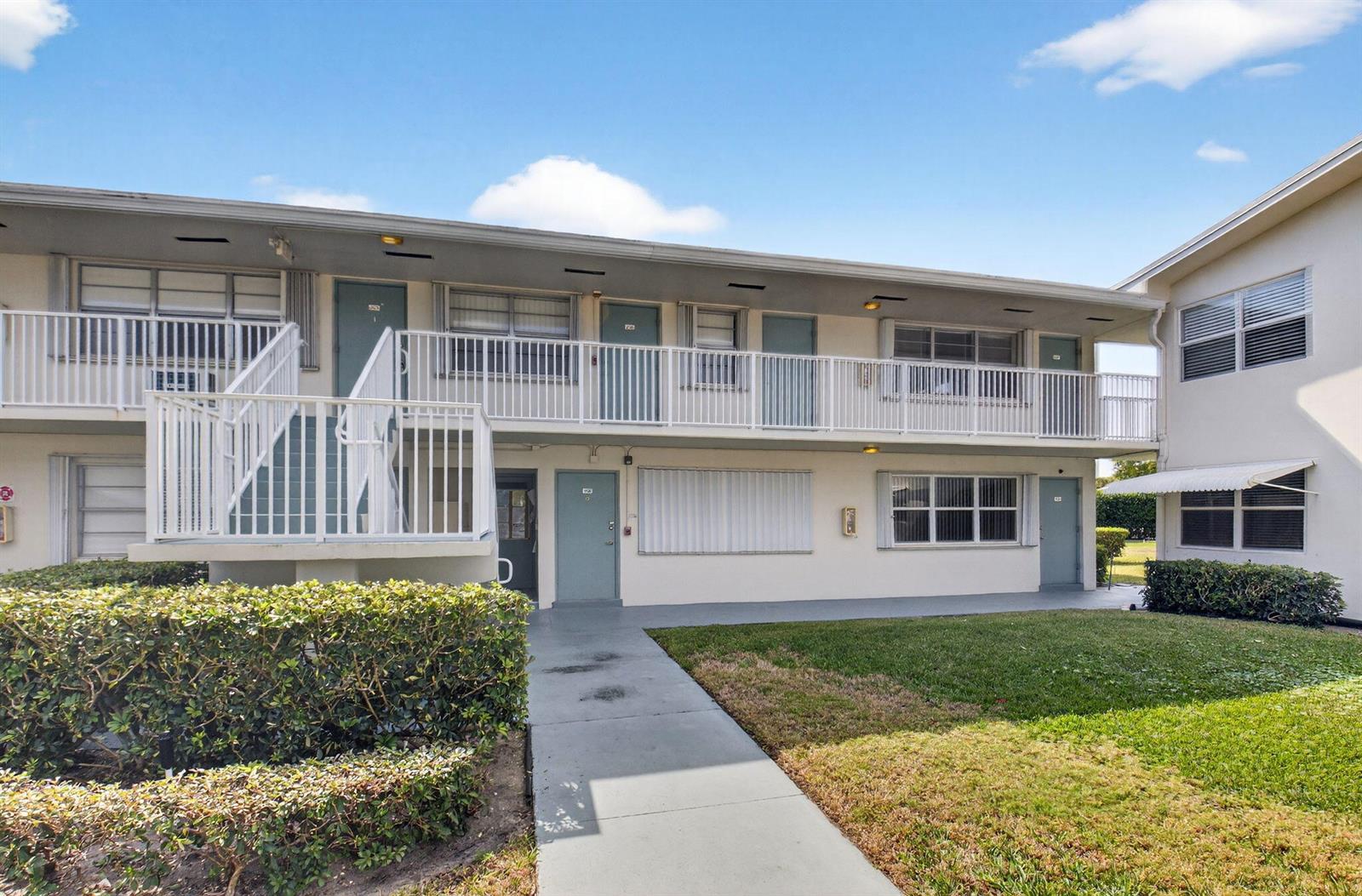 A two-story apartment building exterior features a concrete walkway, white railings, and blue doors — 480 Boynton Beach Boulevard # 204, Boynton Beach FL 33435, BOYNTON BEACH, FL