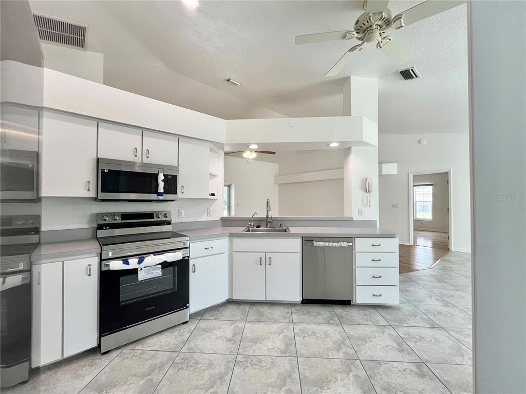 A kitchen with white cabinets, stainless steel appliances, and light-colored tile flooring — 7558 SW 103RD LOOP, OCALA, FL