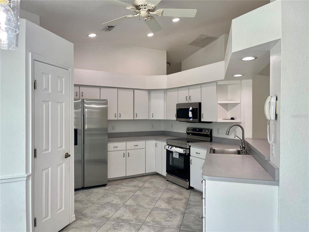 A kitchen features white cabinets, stainless steel appliances, grey countertops, and tile flooring — 7558 SW 103RD LOOP, OCALA, FL