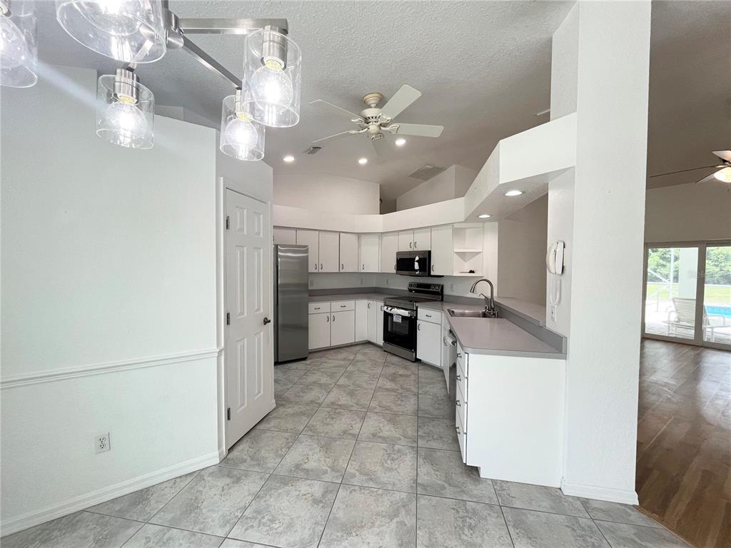 A kitchen with white cabinets, stainless steel appliances, gray countertops, and light tile flooring — 7558 SW 103RD LOOP, OCALA, FL