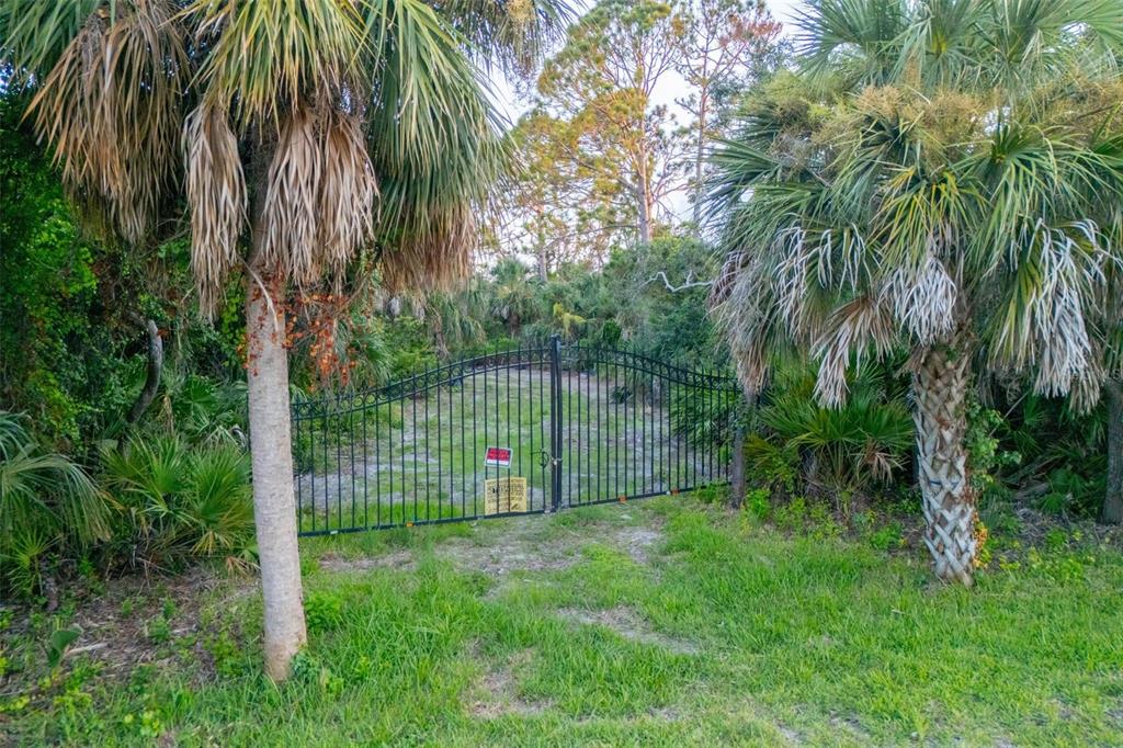 A black metal gate stands between two palm trees at the entrance to a wooded lot — BAYSHORE DRIVE, ENGLEWOOD, FL