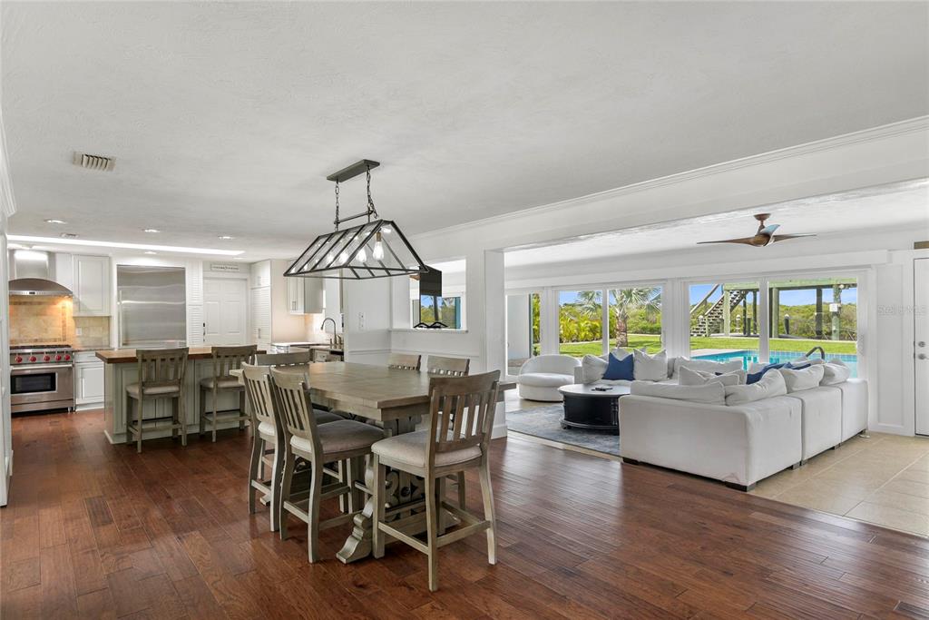 An open-concept kitchen, dining area, and living room with hardwood floors and a backyard pool — 232 QUAY ASSISI, NEW SMYRNA BEACH, FL
