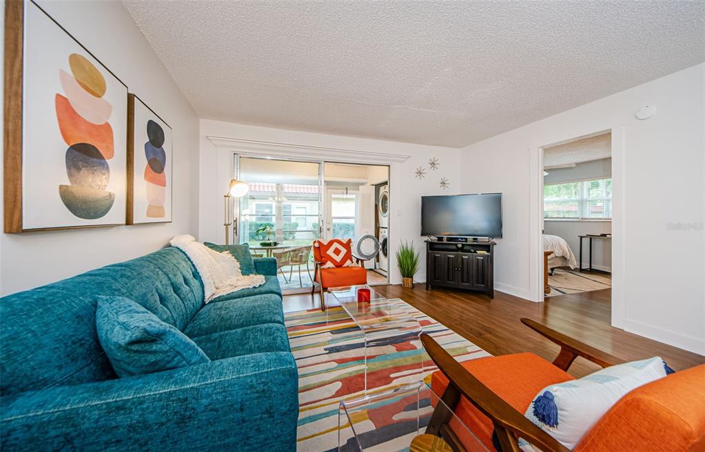 A living room features a teal sofa, orange accent chairs, a colorful rug, and wood flooring — 601 N HERCULES AVENUE UNIT 508, CLEARWATER, FL