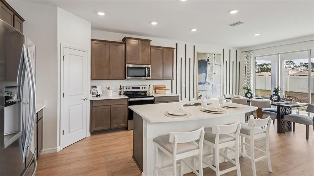 A modern kitchen features dark wood cabinets, a white island with seating, and light flooring — 11823 MEMORIAL DRIVE, BROOKSVILLE, FL