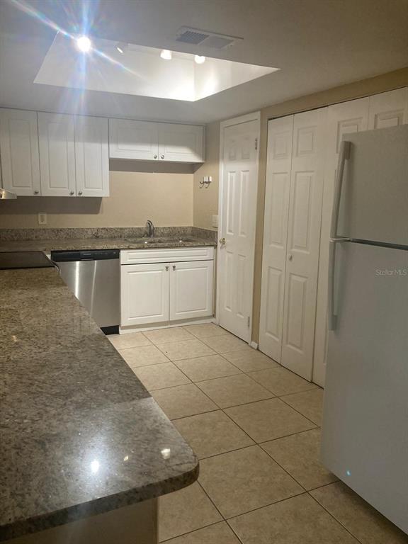 A kitchen features white cabinets, granite countertops, tile flooring, and stainless steel appliances — 9911 TURF COURT UNIT 2, ORLANDO, FL