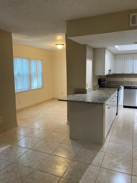 A kitchen with granite countertops and white cabinets opens into a tiled dining area — 9911 TURF COURT UNIT 2, ORLANDO, FL