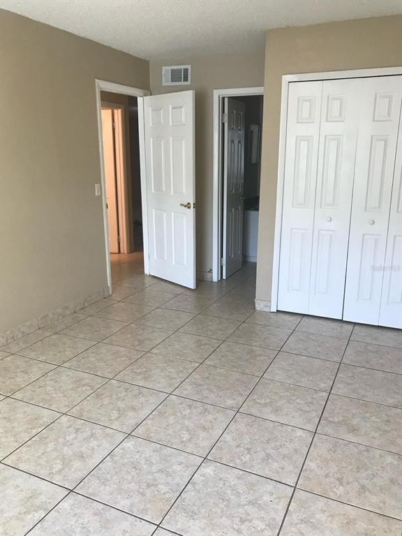 An interior room features light-colored tile flooring, beige walls, two open doorways, and white closet doors — 9911 TURF COURT UNIT 2, ORLANDO, FL