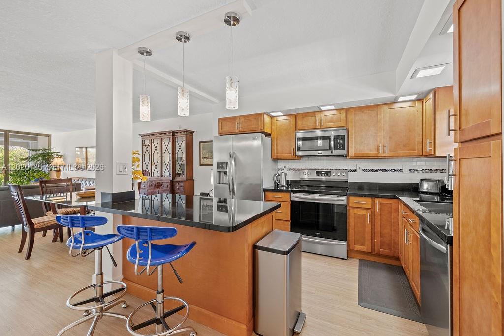 A kitchen features wood cabinets, black countertops, stainless steel appliances, and a breakfast bar — 5300 Highway A1a # 302, Vero Beach FL 32963, VERO BEACH, FL