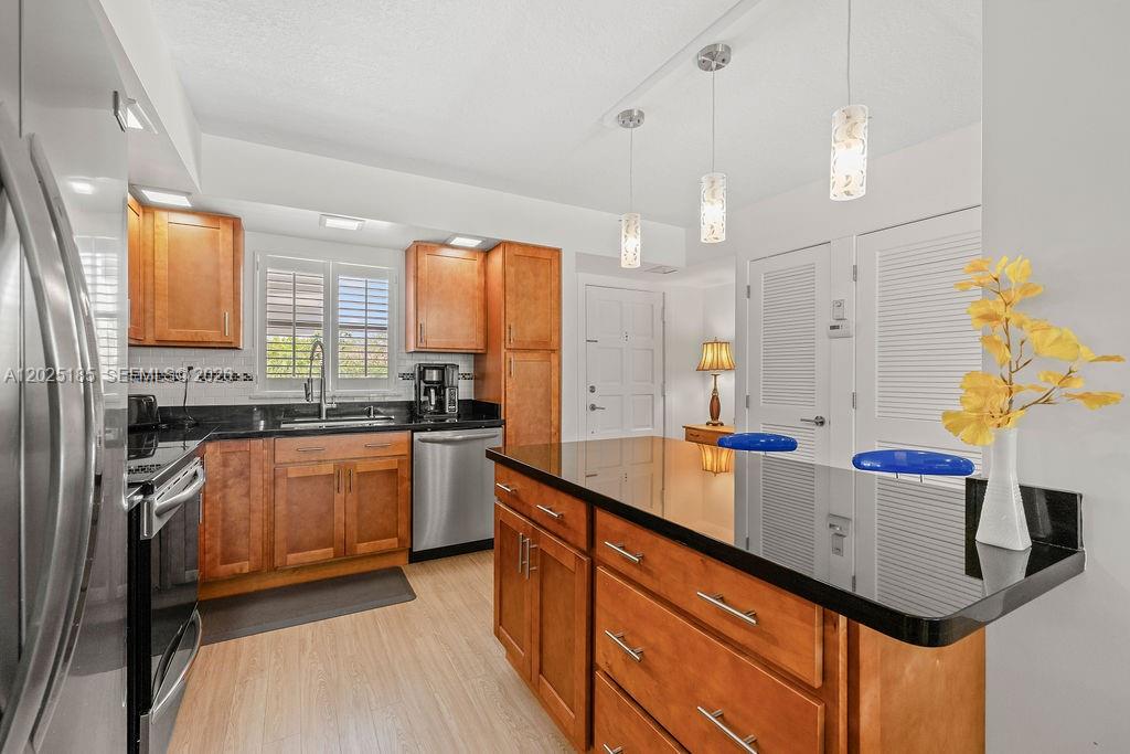 A kitchen features wood cabinets, black countertops, stainless steel appliances, and a central island — 5300 Highway A1a # 302, Vero Beach FL 32963, VERO BEACH, FL