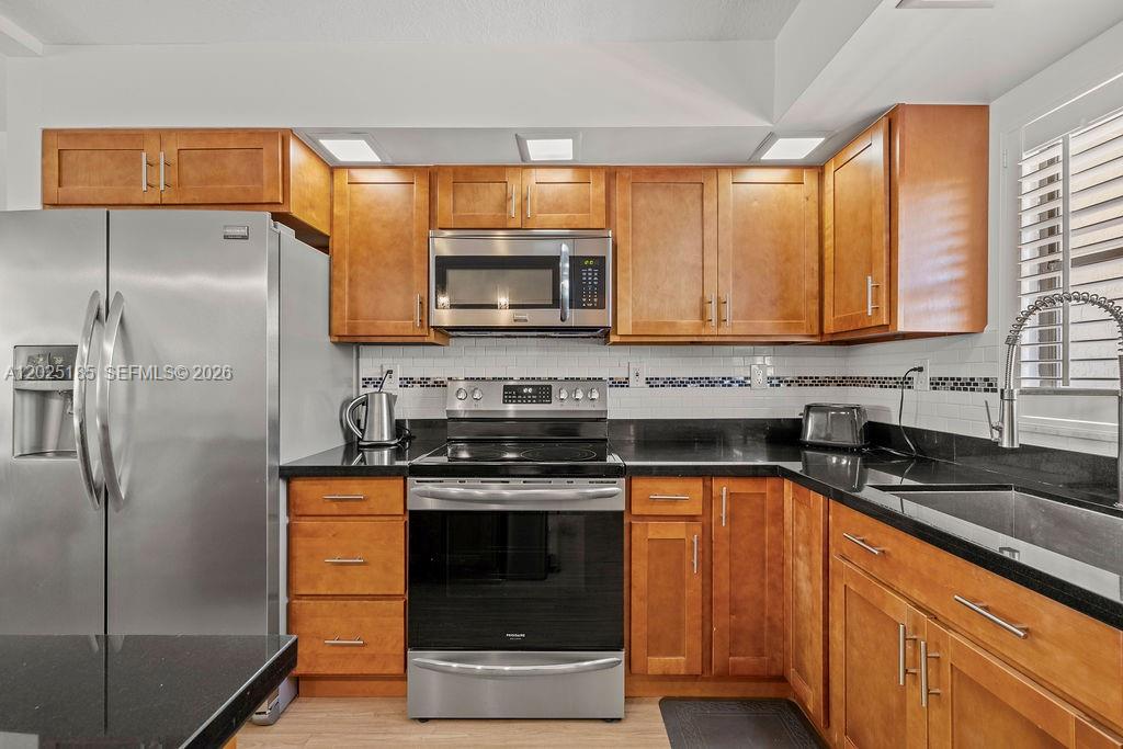A kitchen features wood cabinets, stainless steel appliances, and black countertops with a tiled backsplash — 5300 Highway A1a # 302, Vero Beach FL 32963, VERO BEACH, FL