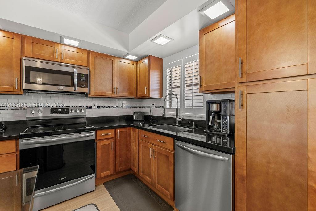 A kitchen features wood cabinets, black countertops, stainless steel appliances, and a white backsplash — 5300 Highway A1a # 302, Vero Beach FL 32963, VERO BEACH, FL