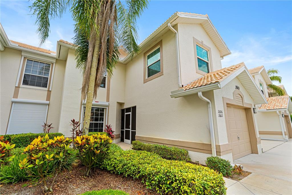 A two-story beige stucco townhouse features a garage, a palm tree, and landscaped bushes — 380 STELLA MARIS DRIVE N UNIT 2602, NAPLES, FL