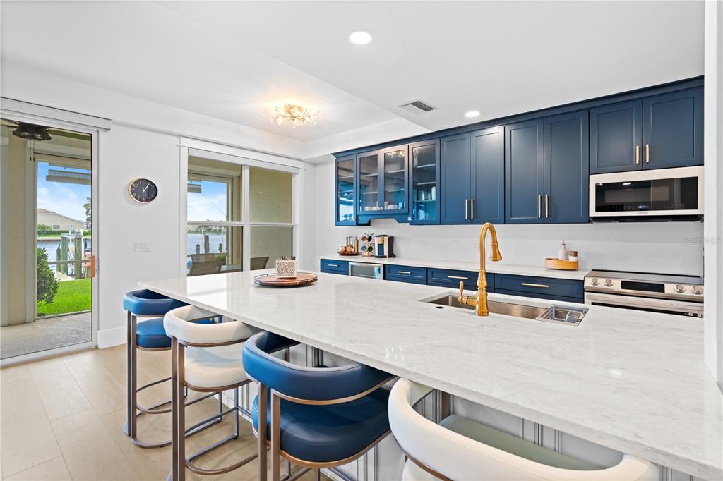 A kitchen features blue cabinets, a white quartz island, and a view of a canal — 380 STELLA MARIS DRIVE N UNIT 2602, NAPLES, FL