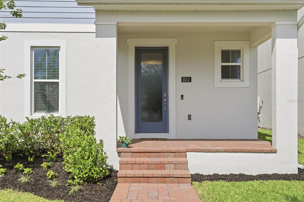 A front porch with brick steps leads to a blue glass-paneled door on a house — 2512 CEDAR ROSE STREET, APOPKA, FL