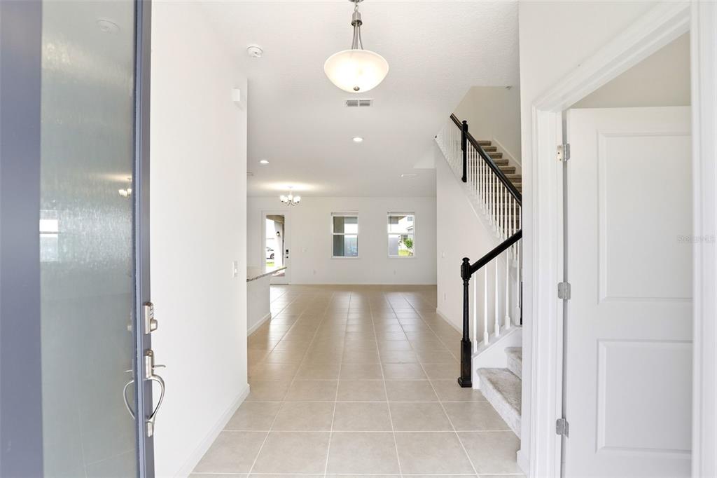 A bright entryway features tile flooring, a staircase with a dark railing, and overhead lighting — 2512 CEDAR ROSE STREET, APOPKA, FL