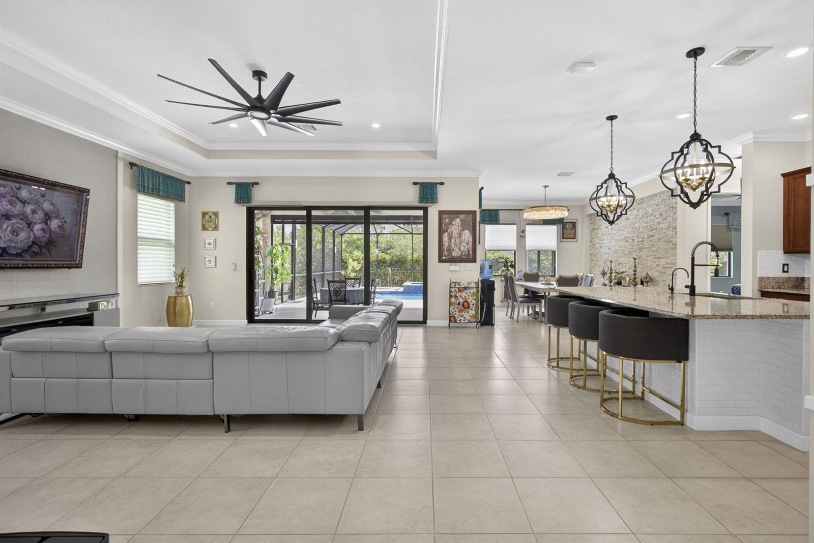 An open-concept living room and kitchen feature tile flooring, a large sectional, and bar seating — 1010 Sweetgrass Street, Loxahatchee FL 33470, LOXAHATCHEE, FL