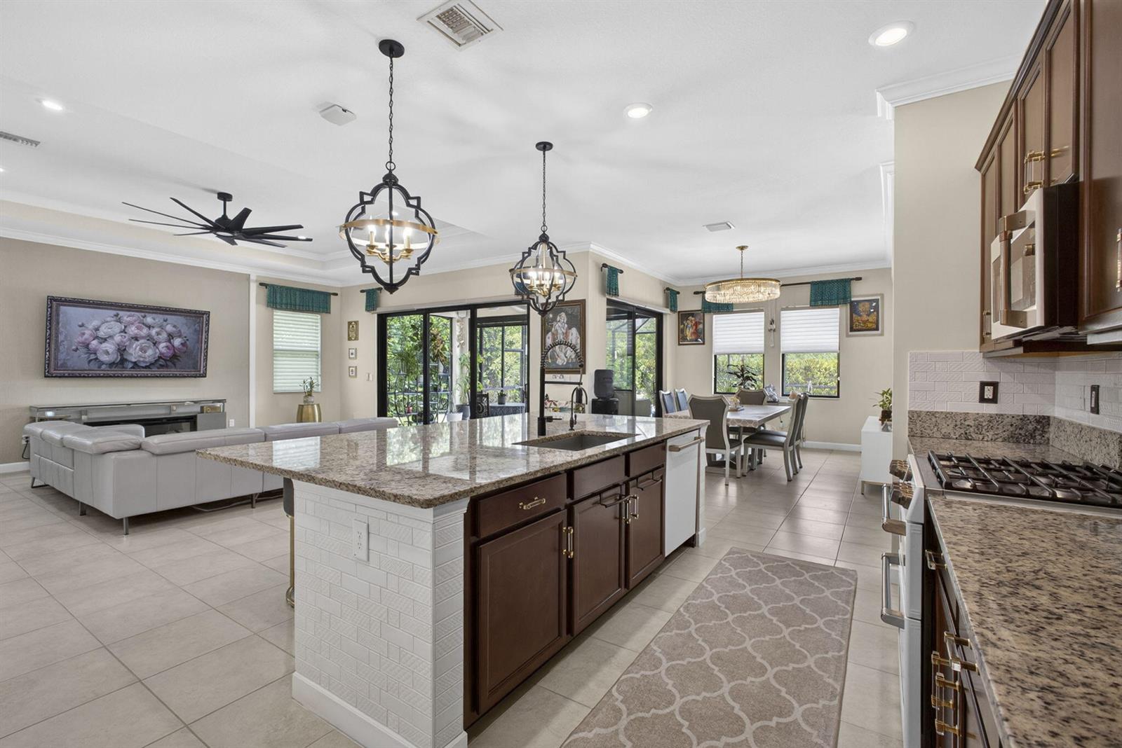 A kitchen with granite countertops and dark wood cabinets overlooks an open-concept living and dining area — 1010 Sweetgrass Street, Loxahatchee FL 33470, LOXAHATCHEE, FL