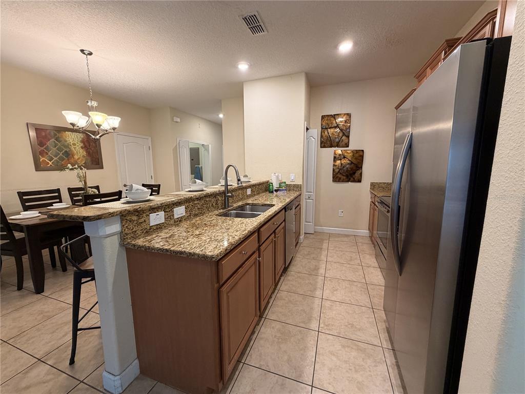 A kitchen with granite countertops, wooden cabinets, and stainless steel appliances overlooks a dining area — 2931 BANANA PALM DRIVE, KISSIMMEE, FL