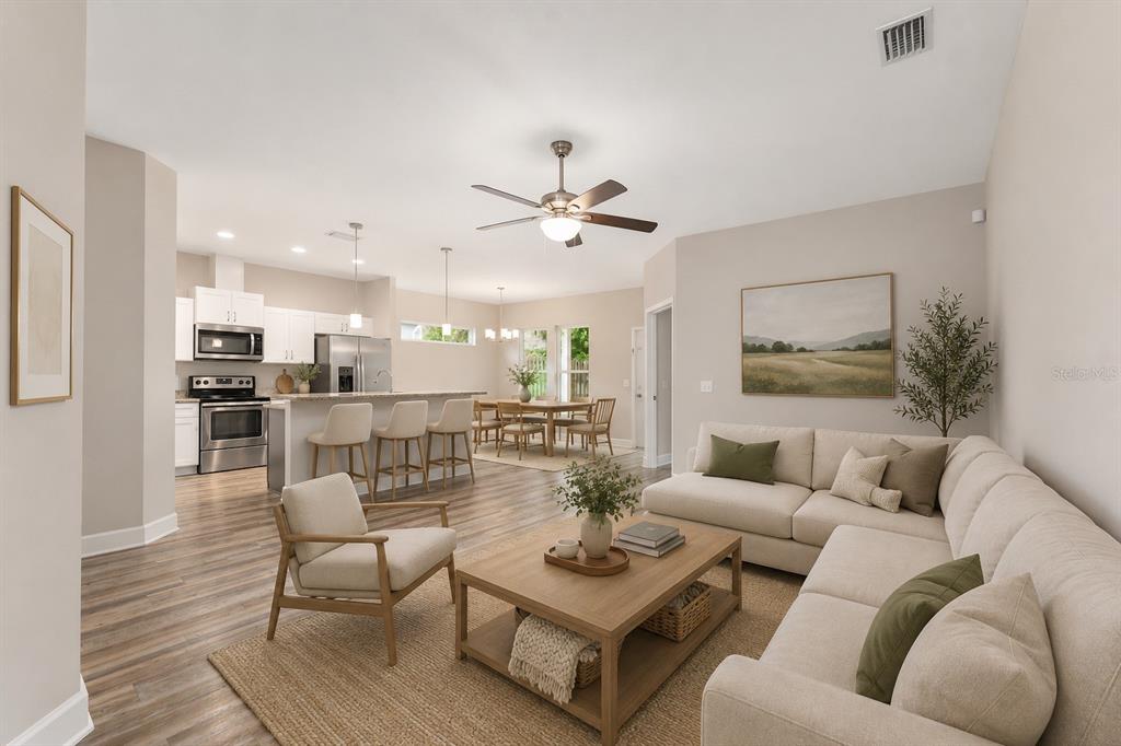 A bright, open-concept living room and kitchen area with light wood flooring and neutral furniture — 12174 NW 162ND DRIVE, ALACHUA, FL