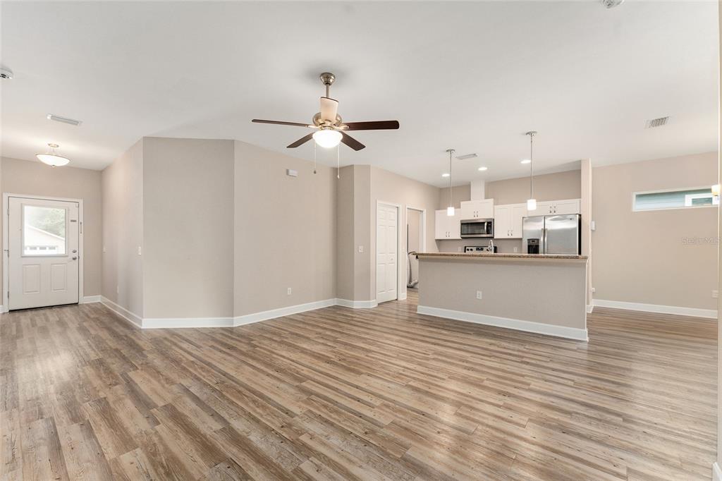 An open-concept living area features light wood-look flooring, a ceiling fan, and a kitchen island — 12174 NW 162ND DRIVE, ALACHUA, FL