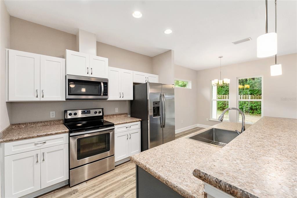 A kitchen features white cabinets, stainless steel appliances, granite countertops, and a large island — 12174 NW 162ND DRIVE, ALACHUA, FL