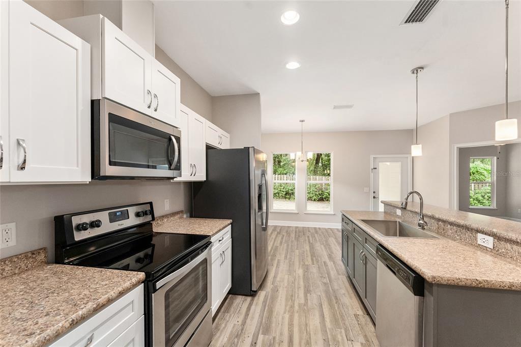 A kitchen features white upper cabinets, gray lower cabinets, stainless steel appliances, and granite countertops — 12174 NW 162ND DRIVE, ALACHUA, FL