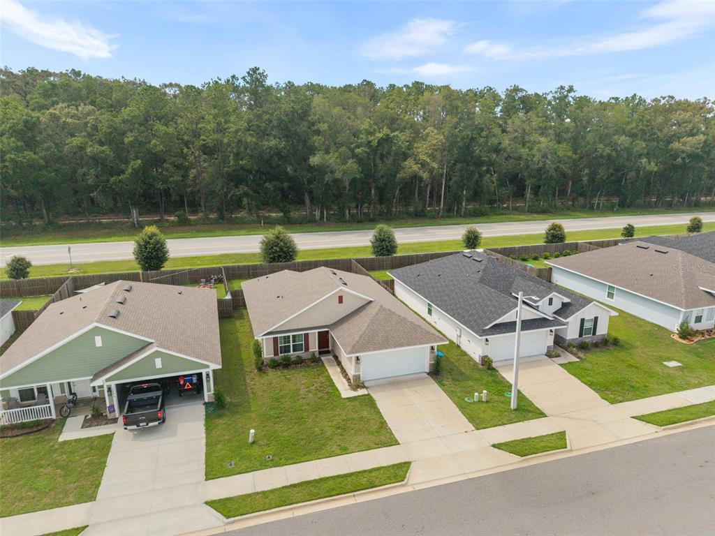 An aerial view shows three suburban houses with driveways and lawns bordering a wooded area — 12692 NW 162ND DRIVE, ALACHUA, FL