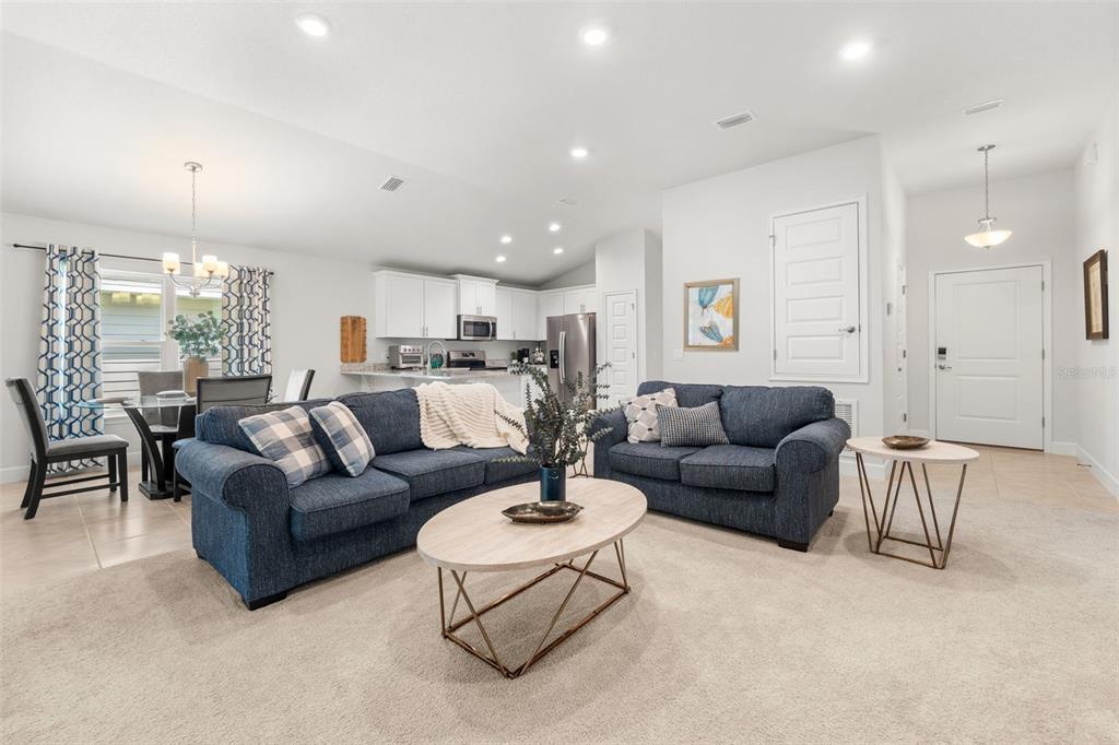 An open-concept living room features blue sofas, a coffee table, and an adjacent kitchen area — 12692 NW 162ND DRIVE, ALACHUA, FL