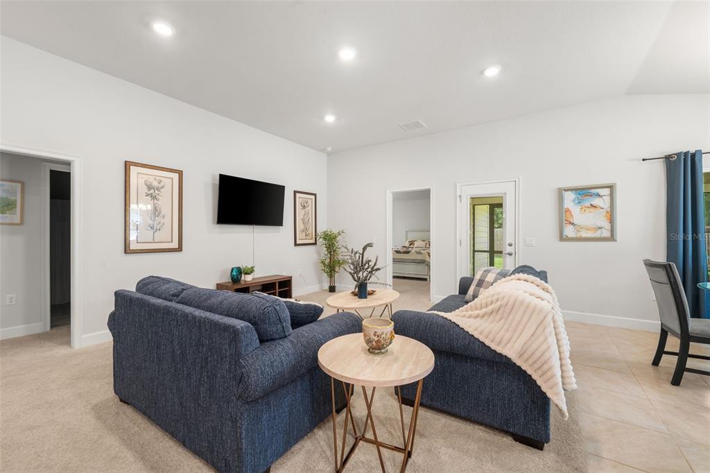 A living room features blue sofas, a television, and neutral carpeting and tile flooring — 12692 NW 162ND DRIVE, ALACHUA, FL