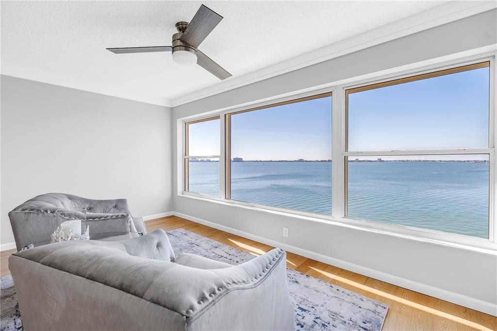 A living room with gray tufted sofas, hardwood floors, and large windows overlooking the water — 6020 SHORE BOULEVARD S UNIT 712, GULFPORT, FL