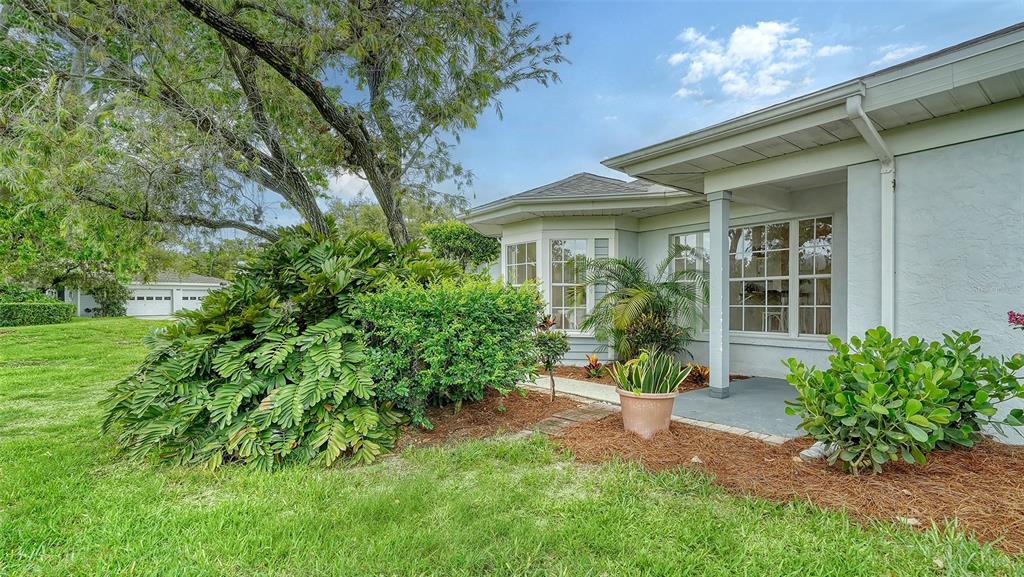 A white house exterior features a bay window, a covered porch, and lush landscaping — 6467 CARRINGTON CIRCLE UNIT 43, SARASOTA, FL