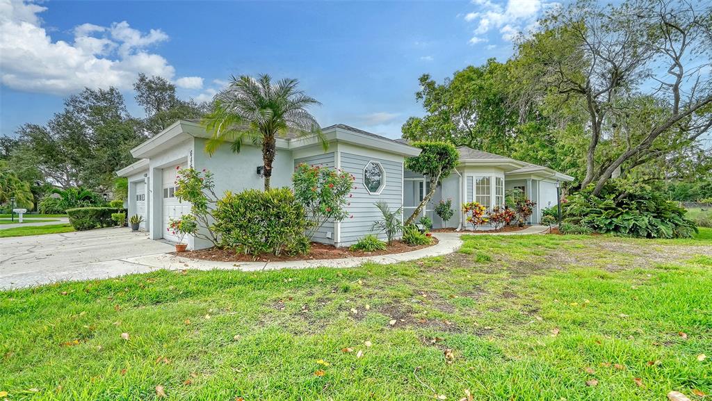 A single-story house with light blue siding, a garage, and a landscaped front yard — 6467 CARRINGTON CIRCLE UNIT 43, SARASOTA, FL