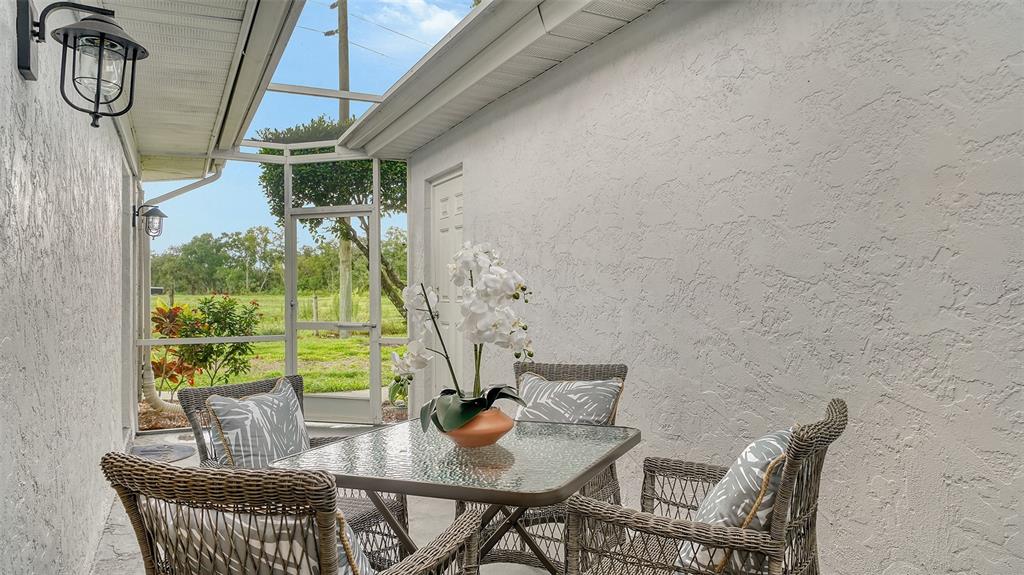 A glass-topped table and wicker chairs sit on a screened-in patio with stucco walls — 6467 CARRINGTON CIRCLE UNIT 43, SARASOTA, FL