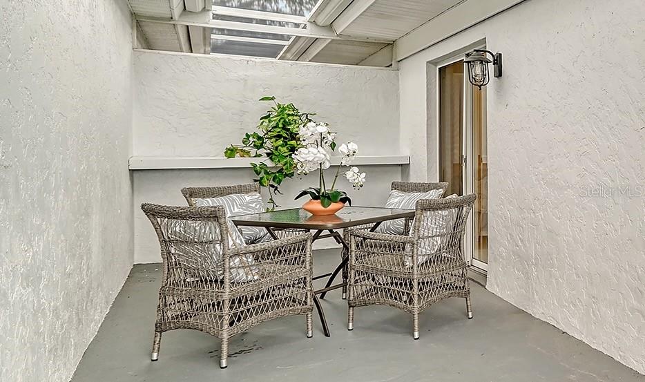 A covered patio features a glass-topped table, four wicker chairs, and a potted orchid — 6467 CARRINGTON CIRCLE UNIT 43, SARASOTA, FL