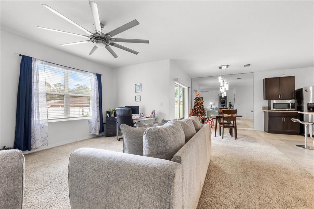 A living room with a ceiling fan, carpeted floors, and an adjacent kitchen area — 415 FRANCISCO WAY, KISSIMMEE, FL