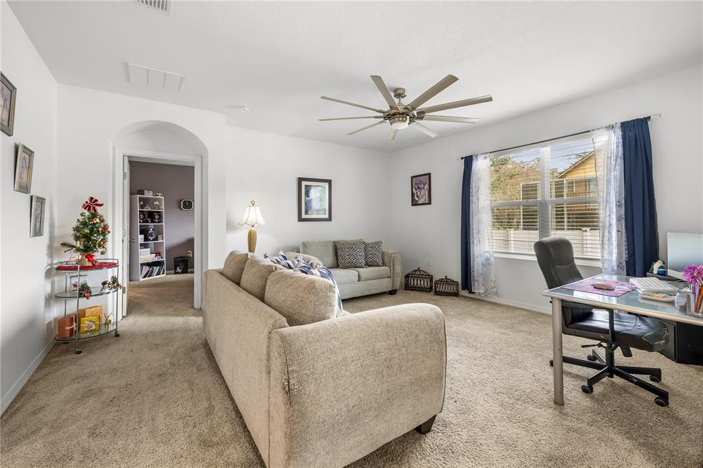 A carpeted living room features a sofa, a desk, and a ceiling fan — 415 FRANCISCO WAY, KISSIMMEE, FL
