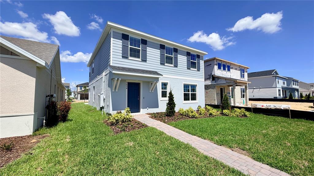 A two-story light blue house with a paved walkway and a neighboring house under construction — 5694 ENCHANTED MEADOW ALLEY UNIT A, CLERMONT, FL