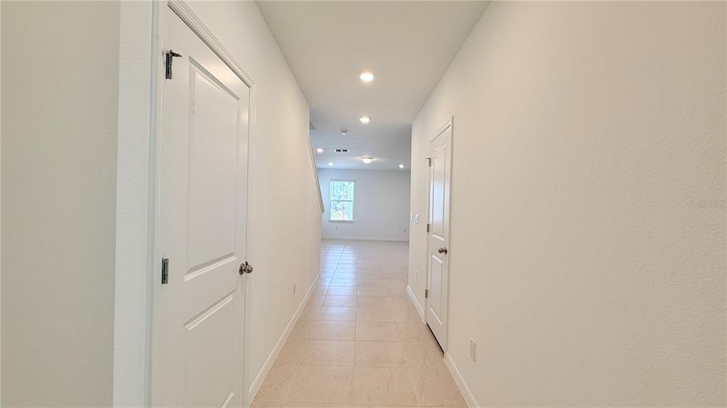 A bright hallway with light tile flooring leads toward a window in the distance — 5694 ENCHANTED MEADOW ALLEY UNIT A, CLERMONT, FL
