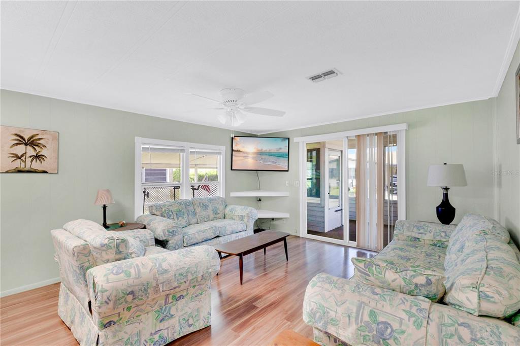 A living room features light green walls, wood-look flooring, floral sofas, and a ceiling fan — 2527 LONGPINE LANE, ST CLOUD, FL