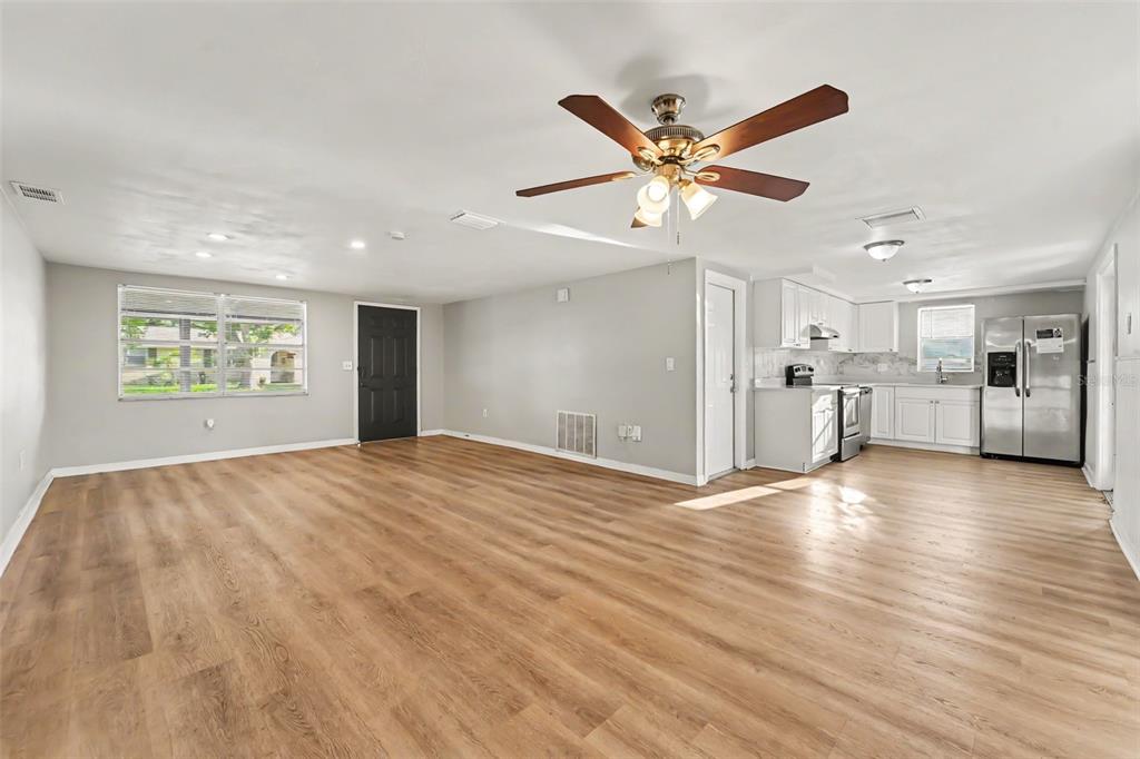 An open-concept living room and kitchen featuring light wood-look flooring and white cabinetry — 7207 SANDALWOOD DRIVE, PORT RICHEY, FL
