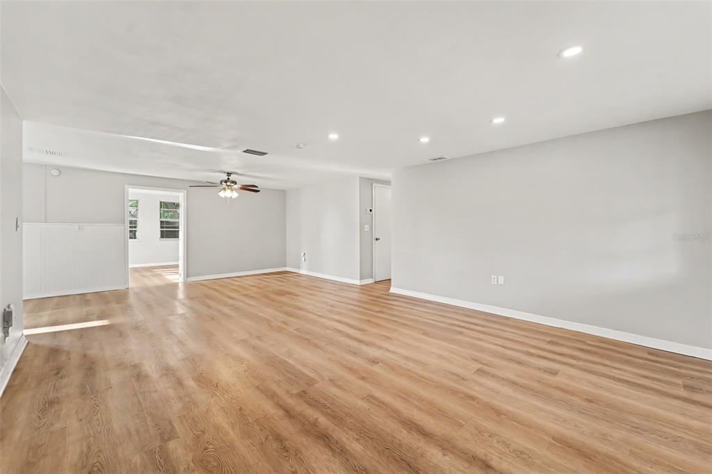 A spacious, empty living room features light wood-look flooring, recessed lighting, and a ceiling fan — 7207 SANDALWOOD DRIVE, PORT RICHEY, FL